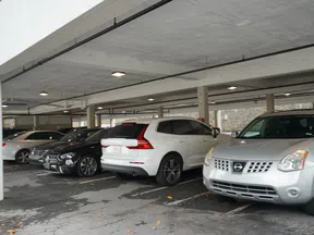 Cars parked in an indoor parking garage with concrete ceiling and pillars, showing various car models and colors.