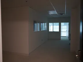 Dimly lit office hallway with framed pictures on the wall and large windows at the end with blinds.