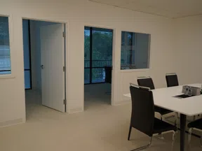 Modern office room with white walls, black chairs around a table, and open doors showing adjacent rooms.