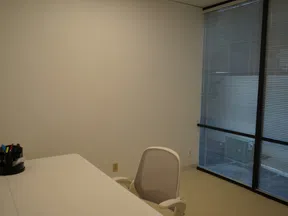 Minimalist office with white desk, ergonomic chair, pen holder, and large windows with blinds.