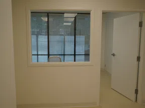 Empty office space with a glass window showing a chair and an open door leading to another room.