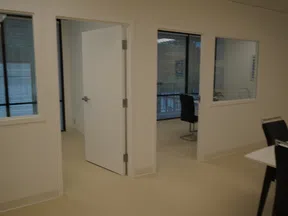 Interior office space with open white doors, glass windows, black chairs, and beige flooring in a modern setting