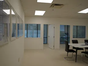 Bright office space with white walls, framed pictures, windows, and a small meeting area with black chairs and table.