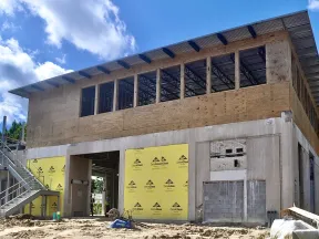 Partially constructed two-story building with plywood upper walls, concrete lower walls, and metal staircase under blue sky.