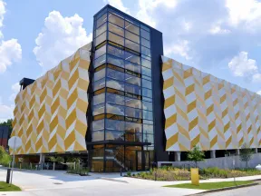 Modern parking garage with geometric yellow and white facade and central glass staircase under a blue sky with clouds.