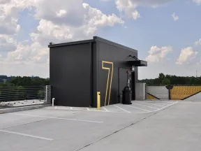Empty rooftop parking lot with a black structure marked with a large yellow number 7 under cloudy blue sky.