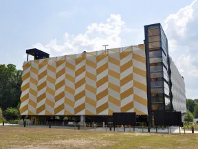 Modern building with yellow and white geometric patterned facade and glass elevator under a partly cloudy sky
