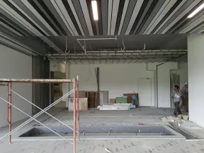 Indoor construction site with ceiling grid, scaffolding, workers, and open floor pit in progress.