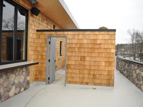 Outdoor patio area with wooden shingle walls, stone accents, glass windows, and a metal door leading inside.