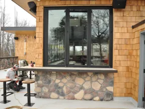 Man working on outdoor seating area with stone and wood siding during construction or renovation.