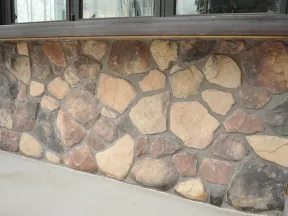 Rustic stone wall facade with various shades of brown and gray stones under a wooden ledge.