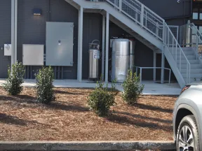 Small shrubs planted in mulch bed outside industrial building with metal stairs and utility tanks nearby