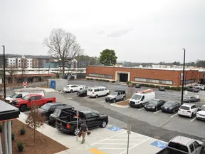 Urban parking lot with various vehicles, including trucks and vans, in front of a brick commercial building on a cloudy day.