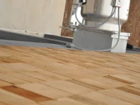 Close-up of a wooden shingle roof with part of a rooftop air conditioning unit in the background.