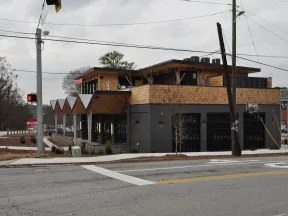 Modern two-story building with wooden accents and large windows on a cloudy day at a street corner.