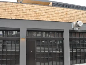 Modern commercial building facade with large grid windows, dark door, gray stucco, and wooden shingle trim.