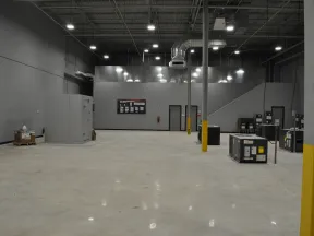 Large empty industrial warehouse space with gray walls, concrete floor, and scattered HVAC units under bright ceiling lights