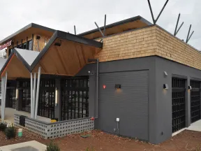Modern restaurant building with black brick walls, large windows, and wooden shingle roofing under gray sky