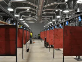 Industrial welding booths with ventilation pipes in a spacious workshop under bright lighting.