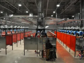 Industrial welding workshop with multiple welding stations separated by orange safety screens and equipped with blue welding machines.