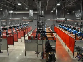 Industrial welding station with multiple booths, blue welding machines, red curtains, and workers in a large factory.