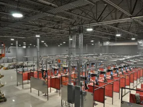 Interior view of a large industrial workshop with multiple welding stations and ventilation ducts under bright lighting