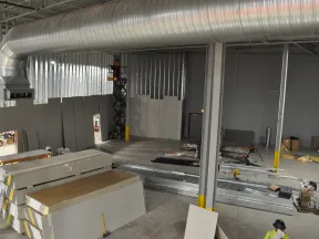 Interior view of a commercial building under construction with drywall stacks, metal framing, and ventilation ducts.