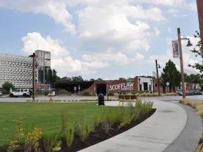 Scofflaw Brewing Co. building with a curved sidewalk, green lawn, flowers, and partly cloudy sky in the background.
