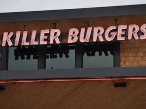 Killer Burgers neon sign mounted on wooden shingle wall above windows at burger restaurant.