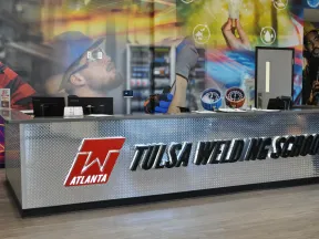 Reception desk with Tulsa Welding School logo and industrial-themed wall mural in modern training center.
