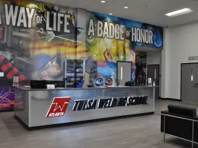 Modern Tulsa Welding School reception with slogan wall art and metal front desk in Atlanta campus lobby