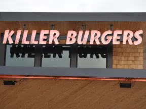 Bright pink neon sign reading Killer Burgers mounted on wooden exterior above windows.