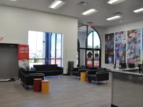 Modern office lounge with black sofas, colorful barrel stools, large windows, and vibrant wall art panels.