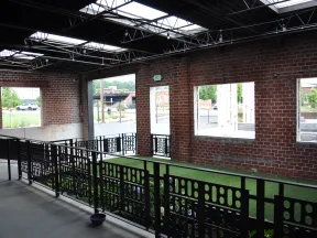 Indoor space with brick walls, large windows, black metal railings, and artificial grass flooring under steel roof beams.