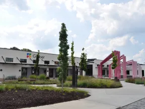 Modern office building with landscaped greenery and pink outdoor architectural installation under a cloudy sky