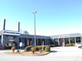 Front view of Tulsa Welding School building with signage, parking lot, and clear blue sky.