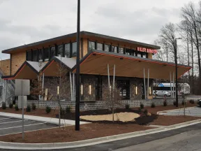 Modern Killer Burger restaurant with sharp angled roof, large windows, and parking lot on a cloudy day