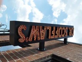 Upside-down vintage marquee sign with light bulbs on a brick building under a blue sky with clouds.