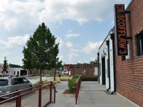 Outdoor sidewalk view of Dr. Scott Law's office with brick walls, trees, parked cars, and partly cloudy sky.