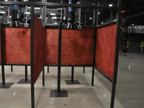Indoor industrial welding booths with red wooden panels and ventilation ducts in factory setting.