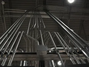 Low angle view of shiny metal electrical conduits running vertically and horizontally across an industrial ceiling.
