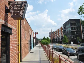 Sidewalk view of Forum Cocktail Company sign on brick building with street and modern apartments in Atlanta