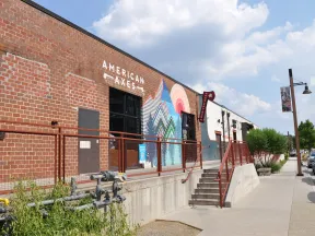 Exterior view of American Axes building with brick wall, colorful mural, and sidewalk under blue sky
