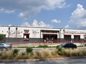 Exterior of Fox Bros Bar-B-Q restaurant with a walk-up window, outdoor seating, and parked cars on a sunny day.