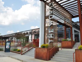 Exterior of a modern building with rust-colored metal structure and stairs under a cloudy sky.