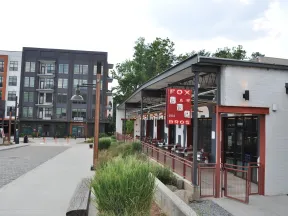 Modern BBQ restaurant with outdoor seating and urban apartment buildings in the background on a bright day.