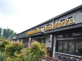 Exterior view of a brick food market with illuminated Food Works sign and greenery in front on a clear day