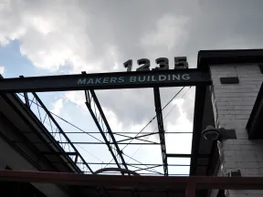 View of the Makers Building entrance with metal framework and address number 1235 against a cloudy sky.
