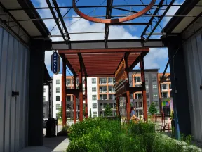 Outdoor modern urban area with metal structures, greenery, and a person walking near apartment buildings on a sunny day