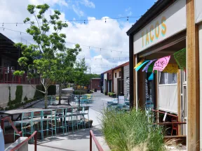 Outdoor seating area of a taco restaurant with colorful decorations and string lights under a bright sky.